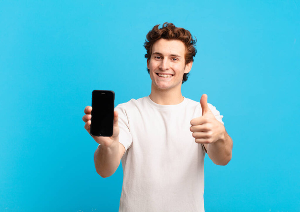 young boy feeling proud, carefree, confident and happy, smiling positively with thumbs up. telephone screen concept - Фото, изображение