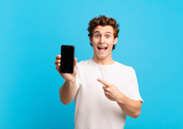 young boy looking excited and surprised pointing to the side and upwards to copy space. telephone screen concept - Φωτογραφία, εικόνα