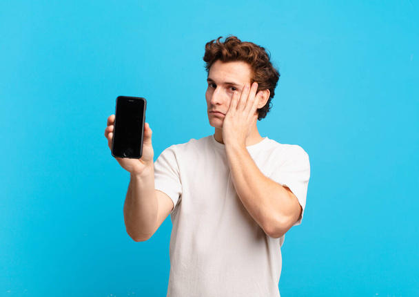 young boy feeling bored, frustrated and sleepy after a tiresome, dull and tedious task, holding face with hand. telephone screen concept - Photo, image