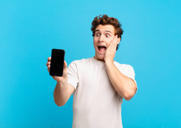 young boy feeling happy, excited and surprised, looking to the side with both hands on face. telephone screen concept - Photo, Image