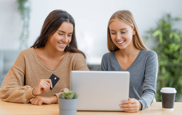 Две счастливые молодые женщины делают онлайн покупки. Девушки делают покупки дома. - Фото, изображение