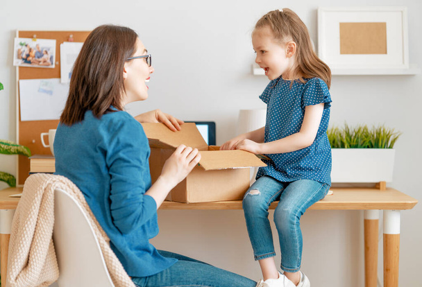 Mother and daughter are unpacking cardboard box at home. - 写真・画像