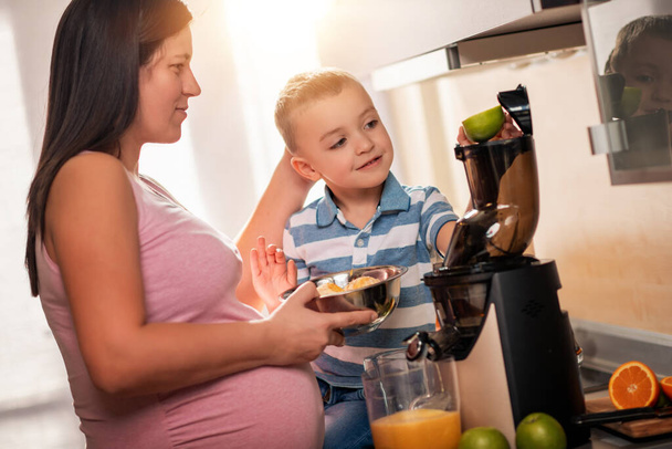 Mujer embarazada y su hijo preparando jugo con frutas frescas. - Foto, imagen