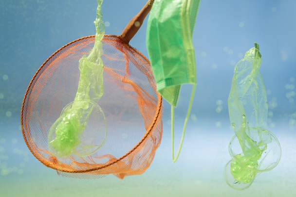 scoop-net perto de máscara médica e sacos de plástico em água, conceito de ecologia - Foto, Imagem