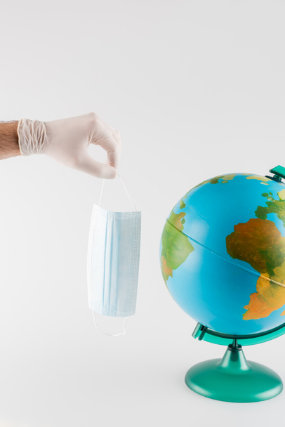 globe near man in latex glove holding medical mask isolated on grey, cropped view, ecology concept - Photo, Image