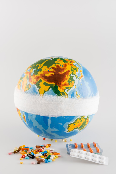 Medikamente nahe bandagiertem Globus auf grauem Hintergrund, ökologisches Konzept - Foto, Bild