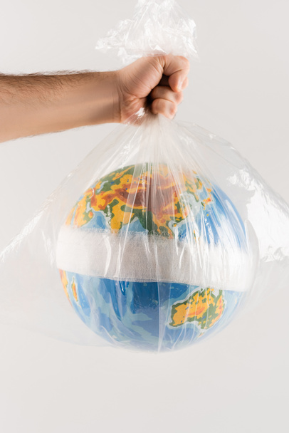 partial view of man holding plastic bag with bandaged globe isolated on grey, ecology concept - Photo, Image