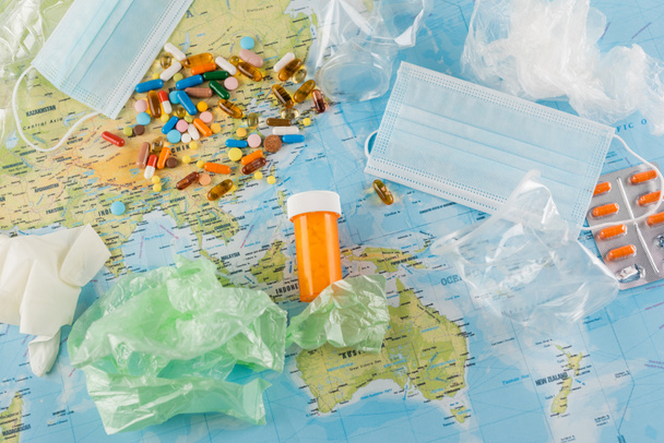 top view pf pills, medical masks and plastic trash on map, ecology concept - Photo, Image