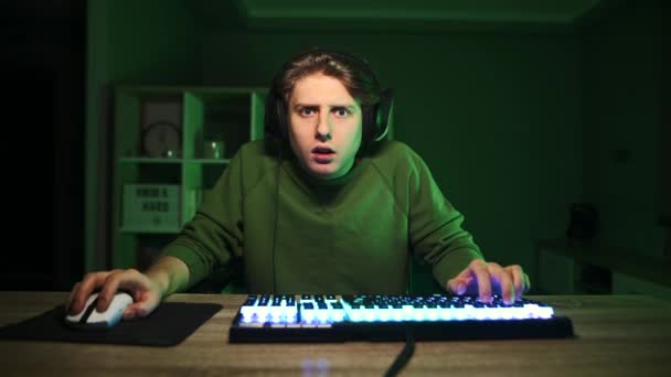 Meglepett fiatal férfi játékos headset játszik videojátékok a számítógépen otthon, és nézi a kamera sokkolt arcát. Érzelmi játék. - Felvétel, videó