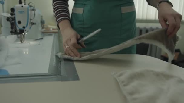 Una mujer en el fondo de una máquina de coser profesional en un taller corta el exceso de tela en los detalles con tijeras - Imágenes, Vídeo