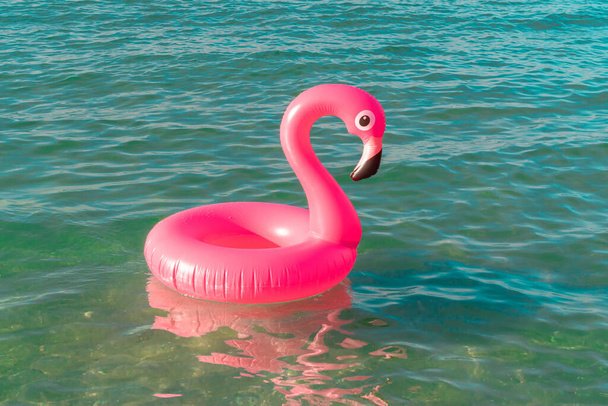 Cartaz de férias de verão. Flamingo inflável rosa na água azul do oceano para o fundo da praia do verão do mar. Brinquedo de pássaro engraçado para crianças - Foto, Imagem