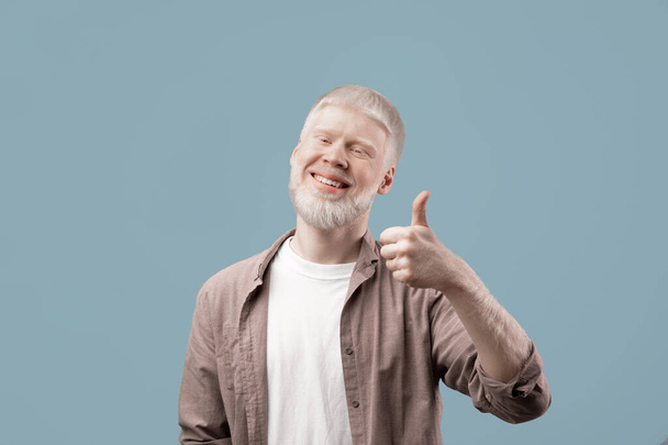 Neşeli albino adam kameraya doğru işaret veriyor, iyi bir şeyi onaylıyor ya da öneriyor. - Fotoğraf, Görsel