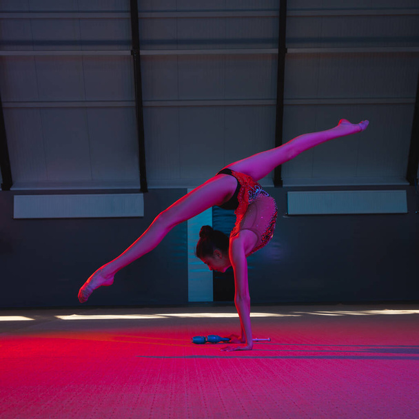 Young female rhythmic gymnast isolated on multicolored background in neon light - Photo, Image