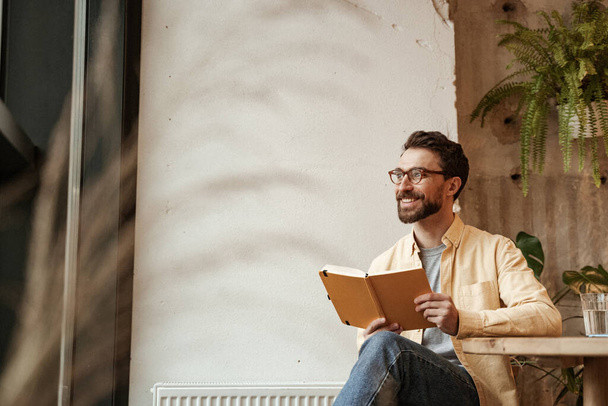 cheerful and bearded man holding notebook and looking away - Photo, Image