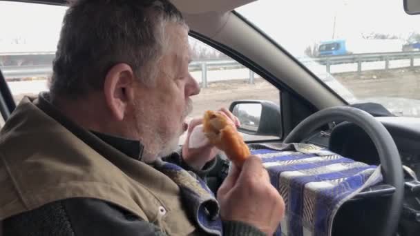 Πεινασμένος λευκός ανώτερος οδηγός τρώει patty ενώ κάθεται μέσα στο αυτοκίνητό του - Πλάνα, βίντεο