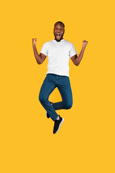Schwarzer Mann schüttelt Fäuste, springt schreiend gestikulierend Ja, gelber Hintergrund - Foto, Bild