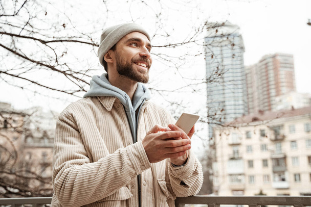 šťastný vousatý muž v čepici drží smartphone  - Fotografie, Obrázek