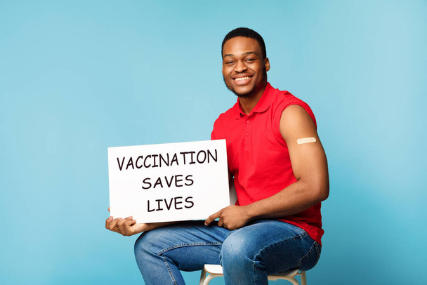 Afrikai Man Holding Board Reklám Covid-19 Vakcina több mint kék háttér - Fotó, kép