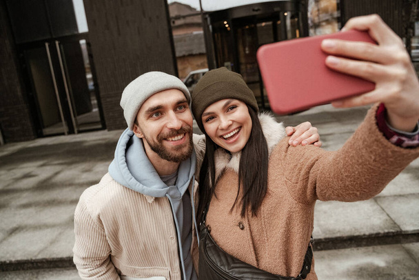 άποψη υψηλής γωνίας του ευτυχισμένου ζευγαριού σε σκούφους beanie λήψη selfie - Φωτογραφία, εικόνα