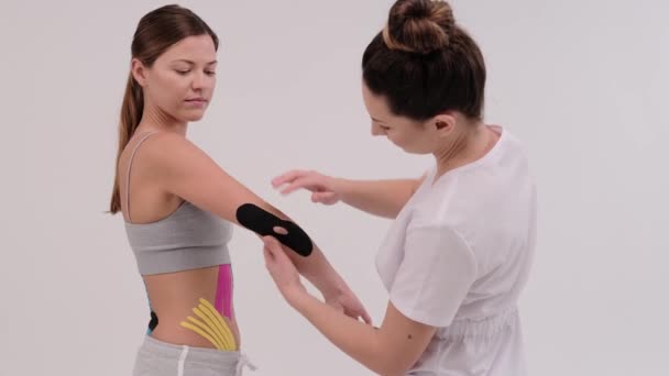 Una fisioterapeuta femenina está midiendo un pedazo de cinesiotape para ser aplicado en una articulación del hombro. Dobla una mano en el codo para comprobar - Metraje, vídeo