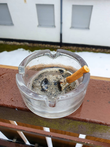 A stubbed out cigarette in an ashtray outside on the balcony. Stop smoking. - Photo, Image