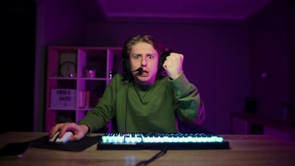 Boze gamer met een gespannen gezicht speelt videospelletjes thuis op een computer in een kamer met paarse lichten en kijkt boos naar de camera. Emotionele man in een headset speelt online games en streaming. - Video
