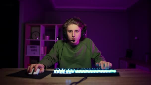 Portret van een slaperige gamer in een headset op zijn hoofd zittend achter een computer en moe kijkend naar het scherm. Calm guy spelen online games 's nachts in de slaapkamer - Video