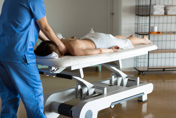 ストレッチャーの上に寝そべっている裸の若い女性、専門の医療マッサージ師や理学療法士は彼女に腰痛のための治療マッサージを与えます。健康と健康の概念. - 写真・画像
