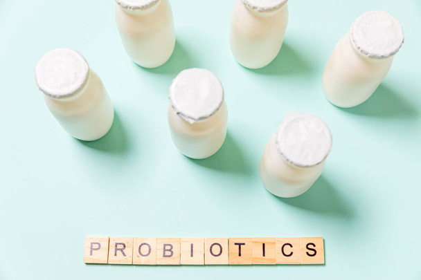 Small bottles with probiotics and prebiotics dairy drink on blue background. Production with biologically active additives. Fermentation and diet healthy food. Bio yogurt with useful microorganisms - Photo, Image