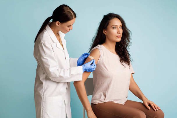Női Doctor Vaccinating Woman alkalmazása ragasztó kötés felett kék háttér - Fotó, kép