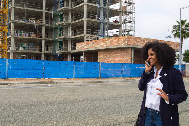 afrikkalais-amerikkalainen nainen rakennuspäällikkö puhuu matkapuhelimella selittää edistymistä rakentamisen rakennusten myöhempää toimitusta asiakkaille. - Valokuva, kuva