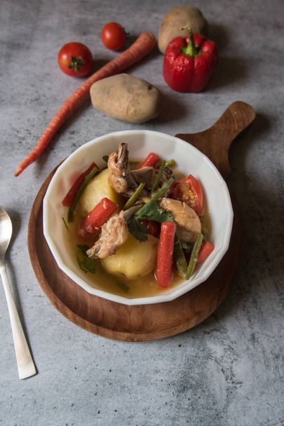  Vue du dessus du ragoût de poulet avec des légumes dans un bol et des condiments crus sur fond. - Photo, image
