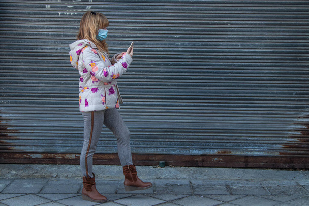 mujer caminando con máscara y teléfono móvil - Foto, Imagen