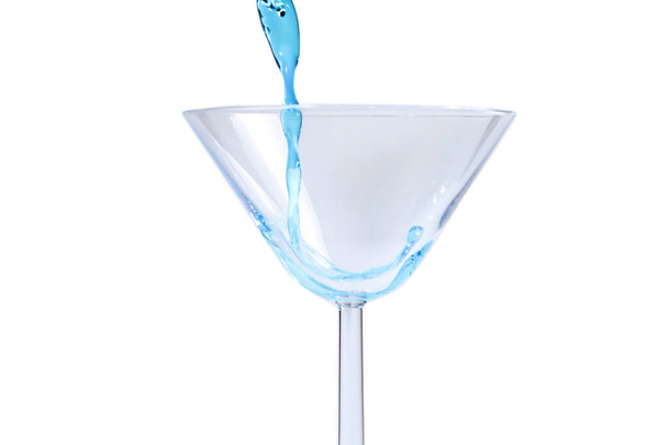 Коктейль з блакитною рідиною в склі. Склянку з блакитною водою заливають рідиною з бризками і краплями. Мартіні скляна начинка з алкоголем з бризками на білому тлі. Концепція освіжаючого напою
.   - Фото, зображення