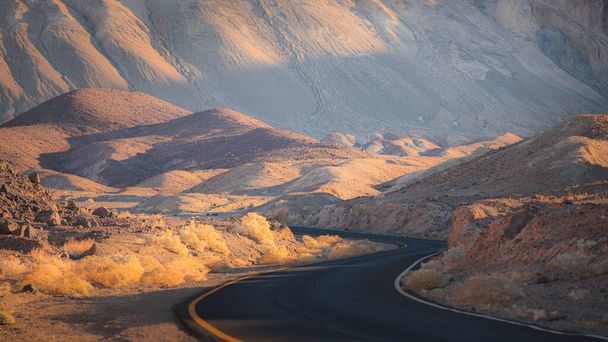 Dramática luz dorada en un camino vacío y sinuoso a través del escarpado terreno del paisaje de las tierras baldías en el Parque Nacional Death Valley Park, EE.UU.. - Foto, imagen