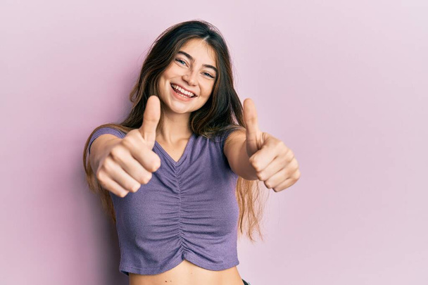 Young caucasian woman wearing casual clothes approving doing positive gesture with hand, thumbs up smiling and happy for success. winner gesture.  - Photo, Image