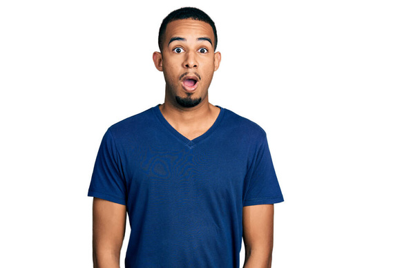 Hombre afroamericano joven vistiendo camiseta casual asustado y sorprendido con la expresión sorpresa, el miedo y la cara emocionada.  - Foto, imagen
