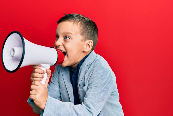 Adorable caucasian boy screaming using megaphone over isolated red background. - 写真・画像