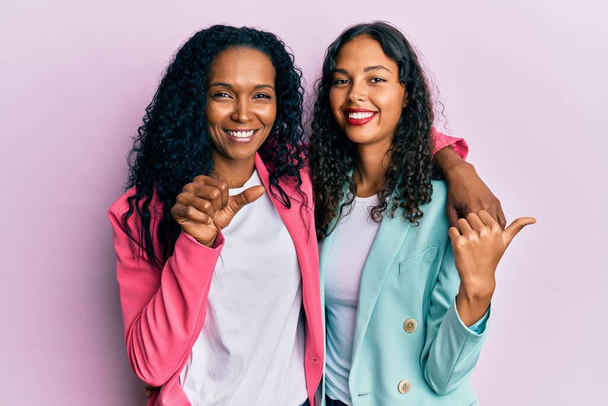 Mãe e filha afro-americana vestindo estilo de negócios apontando para as costas com a mão e os polegares para cima, sorrindo confiante  - Foto, Imagem