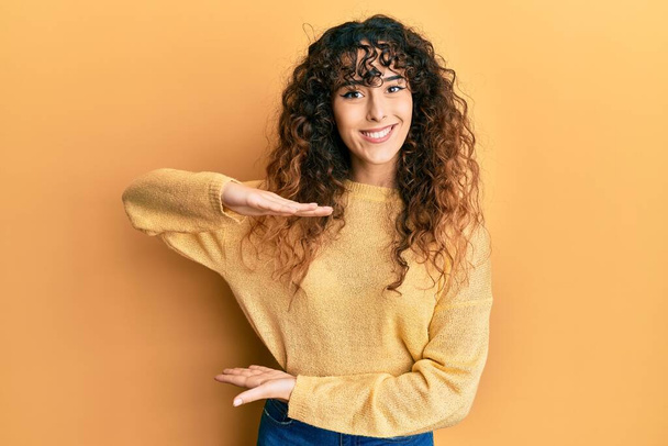 Молодая латиноамериканка в повседневной одежде жестикулирует руками, показывая большой и большой знак, мерный символ. улыбаясь, глядя в камеру. концепция измерения.  - Фото, изображение