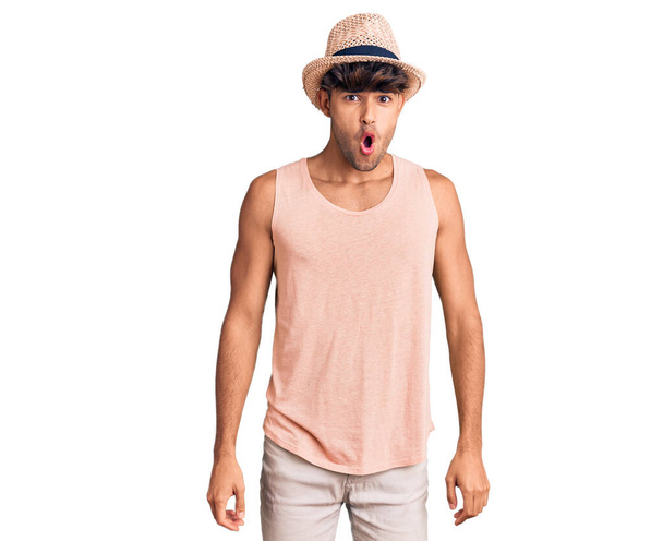 Fiatal spanyol férfi visel nyári kalap fél, és megdöbbent a meglepetés kifejezés, félelem és izgatott arc.  - Fotó, kép