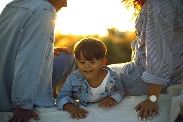 日没に両親と一緒に幸せな子供。森や公園で家族のピクニック。幸せな家族の概念。子供時代と自然。太陽光線と日没 - 写真・画像