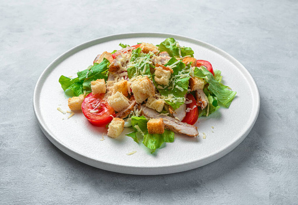 Caesar-Salat auf einem flachen Teller vor grauem Hintergrund. Minimalistischer kulinarischer Hintergrund. Seitenansicht, Nahaufnahme. - Foto, Bild