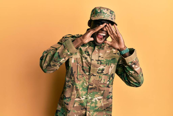 Jovem afro-americano vestindo uniforme do exército gritando zangado em voz alta com as mãos sobre a boca  - Foto, Imagem