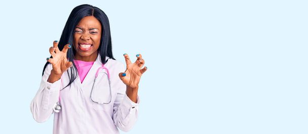 Doktor steteskobu takan genç Afrikalı Amerikalı kadın komik bir şekilde gülümsüyor kedi gibi pençe hareketi yapıyor, agresif ve seksi bir ifade.  - Fotoğraf, Görsel