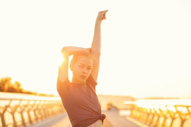 Houkutteleva inkivääri nainen, jolla on urheilullinen runko, käyttää urheiluvaatteita, jotka poseeraavat sillalla auringonnousun aikaan. Tyhjä tila - Valokuva, kuva