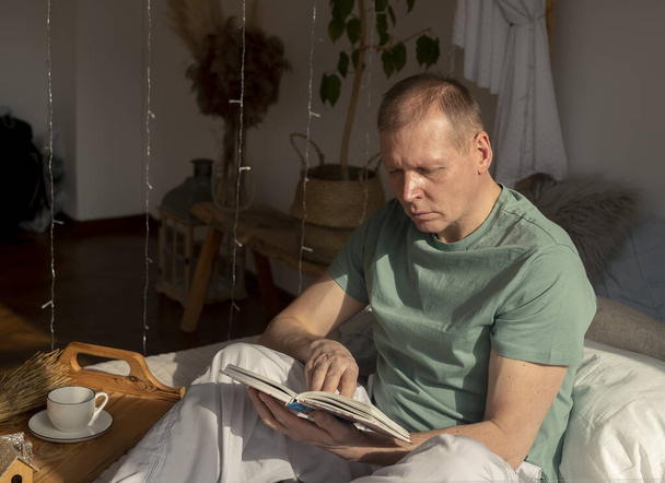 Mature man reading book. Mature person on bed resting. - Fotó, kép