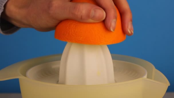 De vrouwenhand perst sap uit sinaasappel op een elektrische sapcentrifuge close-up. Gezond voedselconcept. - Video