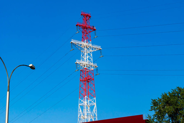 torre de treliça de alta tensão pintada em branco e vermelho, com luzes de emergência e painéis solares fica na cidade - Foto, Imagem