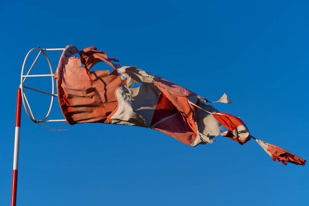Indicador de vento destruído e rasgado contra o céu azul durante o vento forte - Foto, Imagem